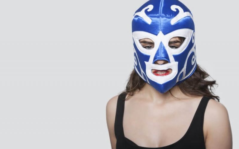 Portrait of a young woman wearing wrestling mask over gray background